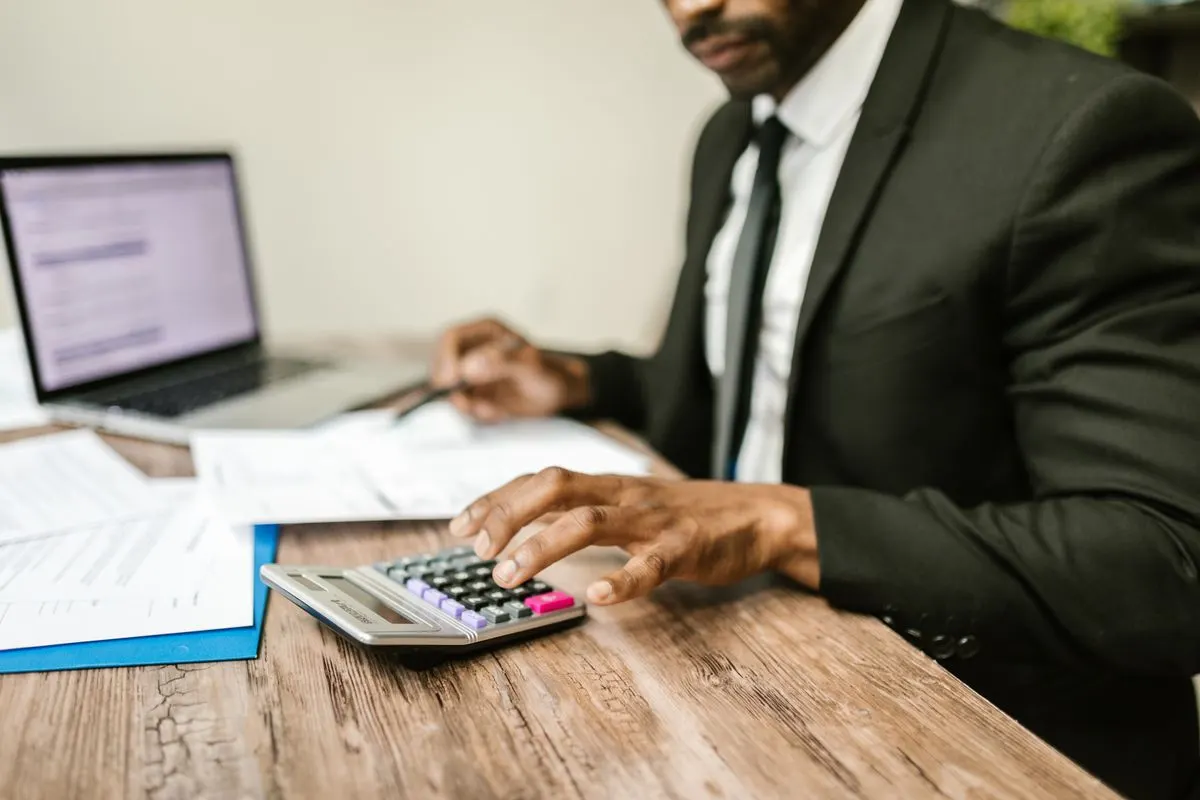 A businessman using a calculator at a desk with financial documents and a laptop